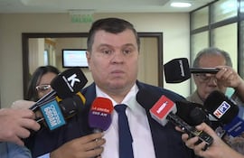 Dionisio Amarilla, con corbata, rodeado de periodistas con micrófonos en un ambiente formal.
