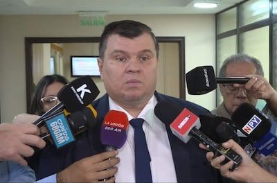 Dionisio Amarilla, con corbata, rodeado de periodistas con micrófonos en un ambiente formal.