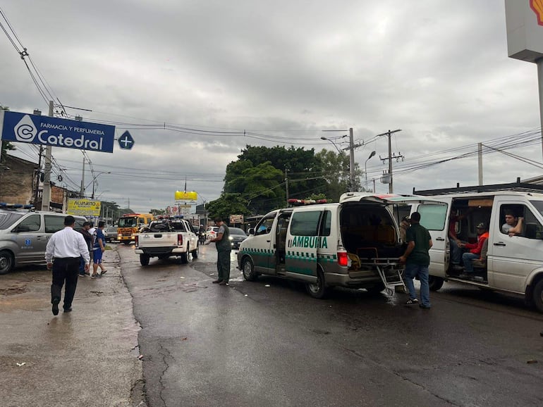 Varios presentes en un accidente con ambulancias. Una persona con camisa blanca se dirige a la ambulancia mientras otros observan.