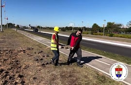 Dos hombres, uno con chaleco y casco amarillos, instalan adoquines junto a una carretera en la Costanera Norte.