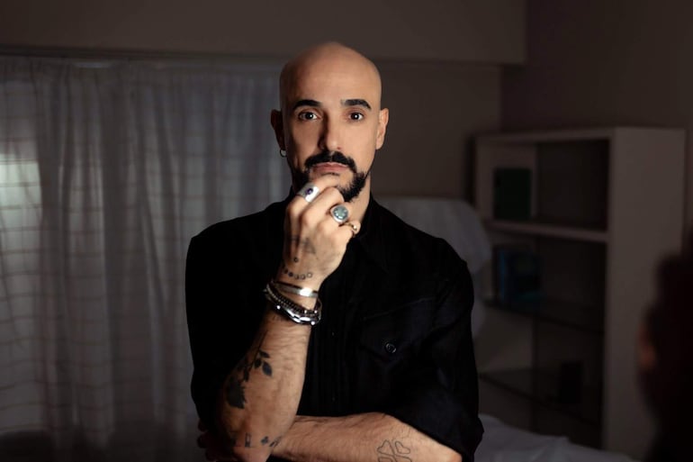 Abel Pintos con camisa negra y barba recortada, en un entorno íntimo y serio, fuauna mano en la barbilla.