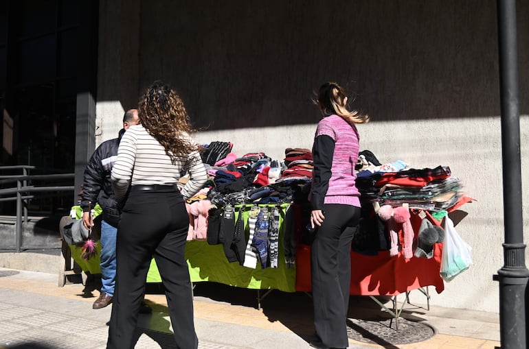 Mujer de espaldas con camiseta de rayas conversa con un hombre en chaqueta oscura, mientras otra mujer en suéter rosa observa prendas.