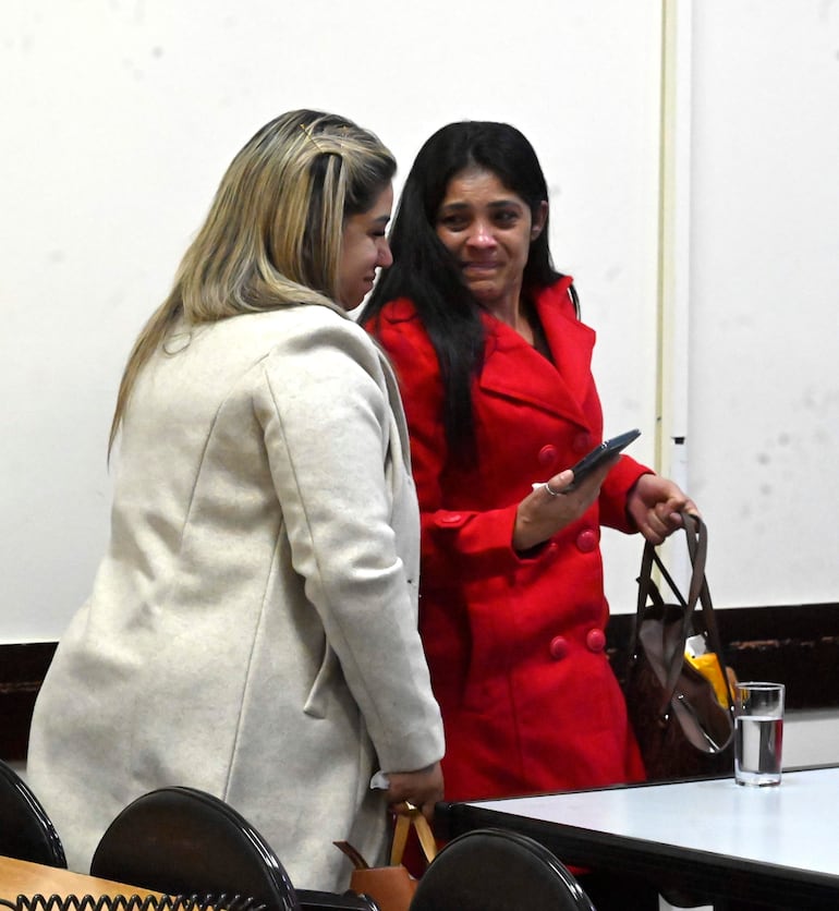 Mujer con abrigo claro y otra en chaqueta roja conversan en ambiente sobrio del Palacio de Justicia.