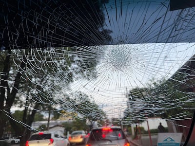 Parabrisas fracturado con grietas visibles, vista desde el interior del vehículo hacia automóviles detenidos en la calle.