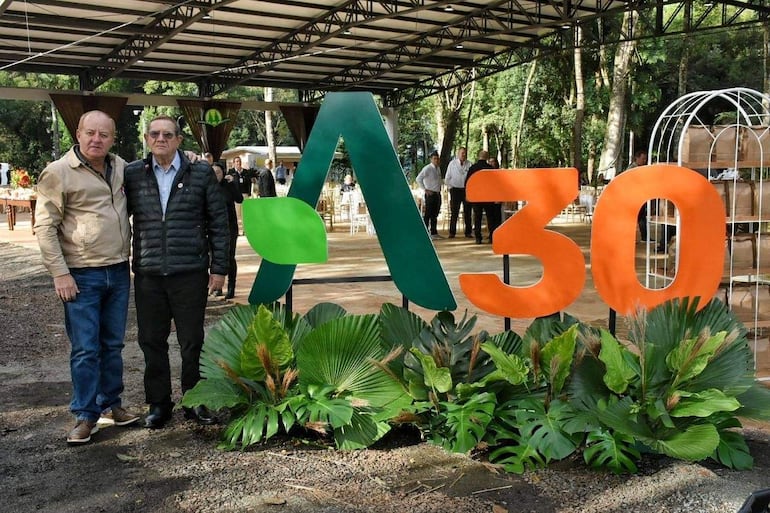 Francisco Javier Pereira Rieve y un hombre mayor posan sonrientes frente al letrero de la Expo Agrodinámica, en un ambiente natural.