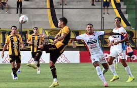 El defensor aurinegro Sebastián Zaracho saca ventaja hacia la pelota a Gaona Lugo. Más atrás, Roque, el autor del gol de la Academia.
