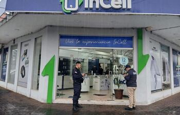 Policía en uniforme frente a la tienda InCell, clima lluvioso con publicidad de productos tecnológicos visible.