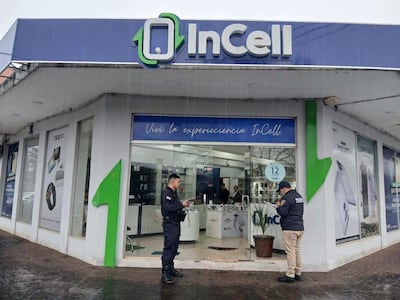 Policía en uniforme frente a la tienda InCell, clima lluvioso con publicidad de productos tecnológicos visible.