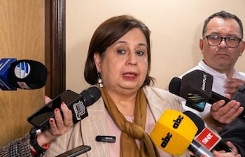 Esperanza Martínez, con blusa clara y abrigo a rayas, responde a preguntas de periodistas en sala de prensa.