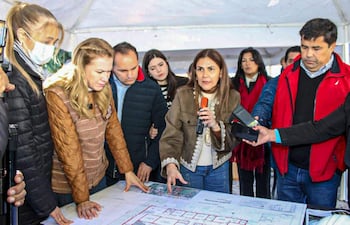María Teresa Barán con micrófono, rodeada de un grupo de personas bajo una carpa, discutiendo un plano en un ambiente exterior.