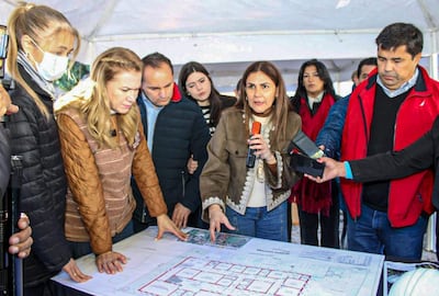 María Teresa Barán con micrófono, rodeada de un grupo de personas bajo una carpa, discutiendo un plano en un ambiente exterior.