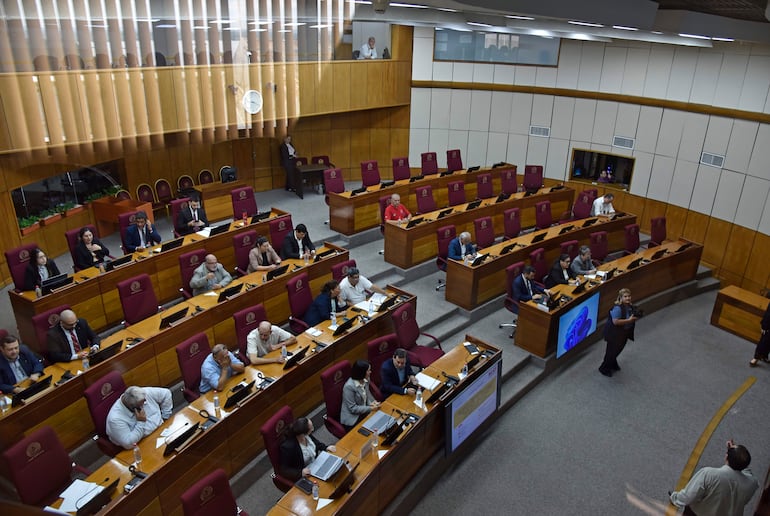 Personas sentadas en bancas formales en un recinto legislativo, observando y tomando apuntes en un ambiente de deliberación política.