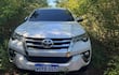 Camioneta Toyota Fortuner blanca parcialmente cubierta por vegetación en un área boscosa, sin personas visibles.