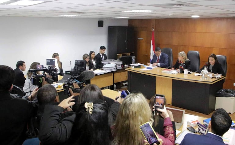 Periodistas capturan el momento del juicio, mientras Rivas, en traje oscuro, se muestra tranquilo en el panel de deliberación.