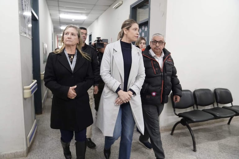 El Dr. Isaías Fretes, vestido con abrigo oscuro, camina por un pasillo acompañado de dos personas en abrigos también oscuros.