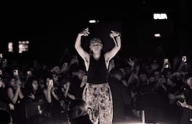 ONEY1 en escenario con camiseta sin mangas y pantalones estampados, levantando un micrófono mientras el público graba con sus teléfonos.