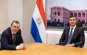 Santiago Peña y Carlos Carvallo Spalding sentados en una mesa, ambos en trajes oscuros y corbatas, con expresiones tranquilas.