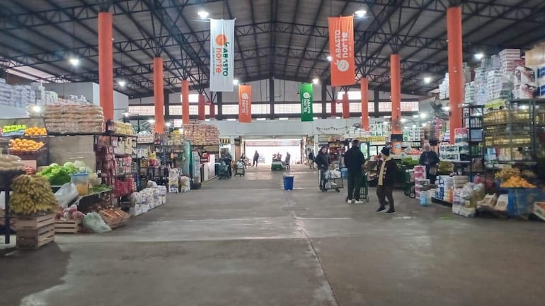 Ambiente animado en el Mercado de Abasto, estanterías llenas de frutas y verduras, y carritos de compras.