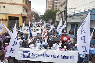 Manifestantes con paraguas y pancartas en apoyo a la Asociación Paraguaya de Enfermería, en un ambiente lluvioso.