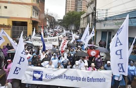 Manifestantes con paraguas y pancartas en apoyo a la Asociación Paraguaya de Enfermería, en un ambiente lluvioso.