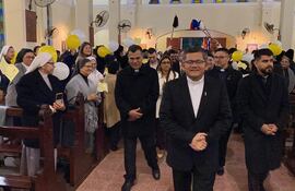 Grupo de personas en trajes oscuros y hábitos religiosos, algunos sosteniendo globos amarillos, en ceremonia dentro de una iglesia.