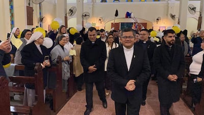 Grupo de personas en trajes oscuros y hábitos religiosos, algunos sosteniendo globos amarillos, en ceremonia dentro de una iglesia.