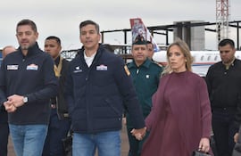 Grupo de seis personas en uniforme, incluido Santiago Peña con abrigo azul, rodeados de aviones en un ambiente formal y tranquilo.