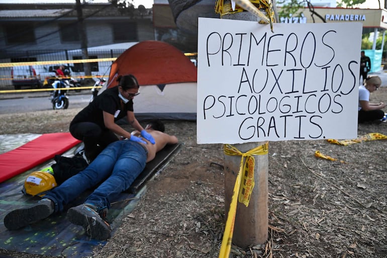Un rescatista recibe un masaje en una zona de recuperación improvisada junto a un letrero que dice "Primeros auxilios psicológicos gratuitos" cerca de los edificios derrumbados tras el terremoto en Cali, Colombia, el 14 de agosto de 2026. (Photo by Raul ARBOLEDA / AFP)