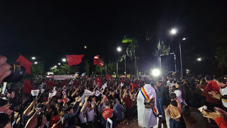 Sebastián Remesowski con capa blanca y banda tricolor, rodeado de multitudes vitoreando y levantando banderas rojas.