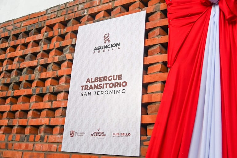 Cartel del Albergue Transitorio San Jerónimo colocado en pared de ladrillos, decorado con cinta roja.