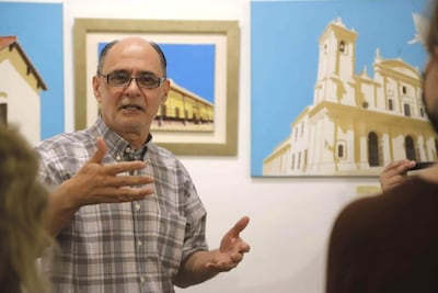 Horacio Guimaraens, hombre mayor con cabello canoso y gafas, gesticula mientras habla, rodeado de cuadros en una galería.