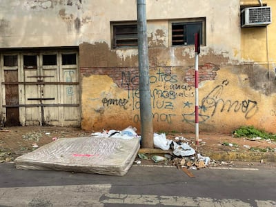 Escena urbana de Asunción con colchón desechado y basura en las veredas, ambiente deteriorado y grafitis visibles en las paredes.