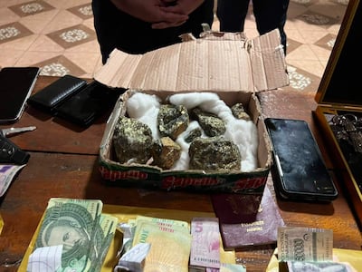 Entorno interior con caja de cartón, pasaporte, billetes y teléfonos móviles, indicando operación de seguridad en curso.