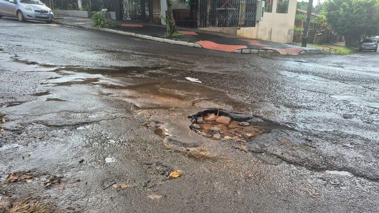 Una calle en mal estado muestra un bache con piedras y agua, reflejando la falta de mantenimiento urbano.