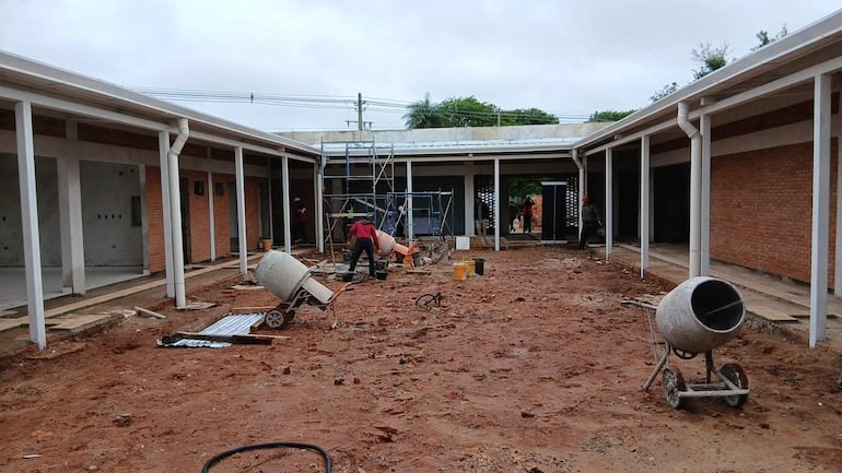 Varios trabajadores en ropa de construcción, utilizando hormigonera y carretillas en un terreno de obra en San Juan Bautista.