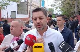 Pedro Alliana con camisa blanca, rodeado de micrófonos y periodistas, en un ambiente exterior con vegetación.