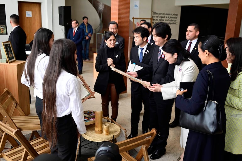 Adriana Ortiz Semidei y Enrique Alfonso conversan con jóvenes en camisas blancas, presentando un objeto decorativo en un ambiente formal.