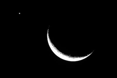 Luna creciente iluminada en el lado derecho del cielo oscuro, junto a un brillo estelar a la izquierda.