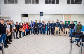 Grupo de 16 personas en fila, con vestimenta formal y casual, en un ambiente administrativo con sillas azules.