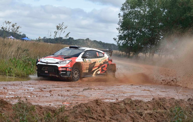 Auto de rally en colores rojo y blanco, con el logo de Petrobras, levantando polvo en un ambiente rural.