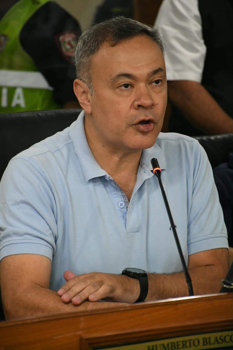 Humberto Blasco sentado en conferencia, con camiseta celeste y expresión concentrada, hablando ante el micrófono.