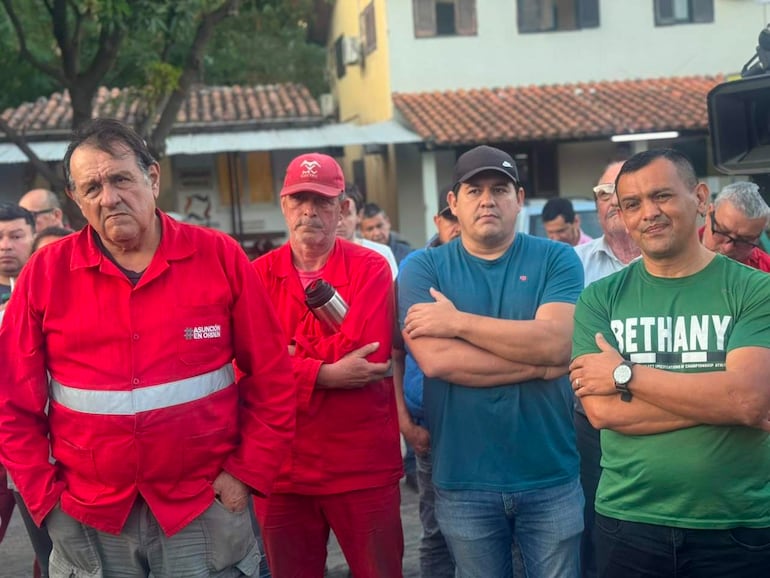 Óscar Pérez, en camisa roja con inscripción, junto a hombres de trabajo serios en ambiente comunitario.