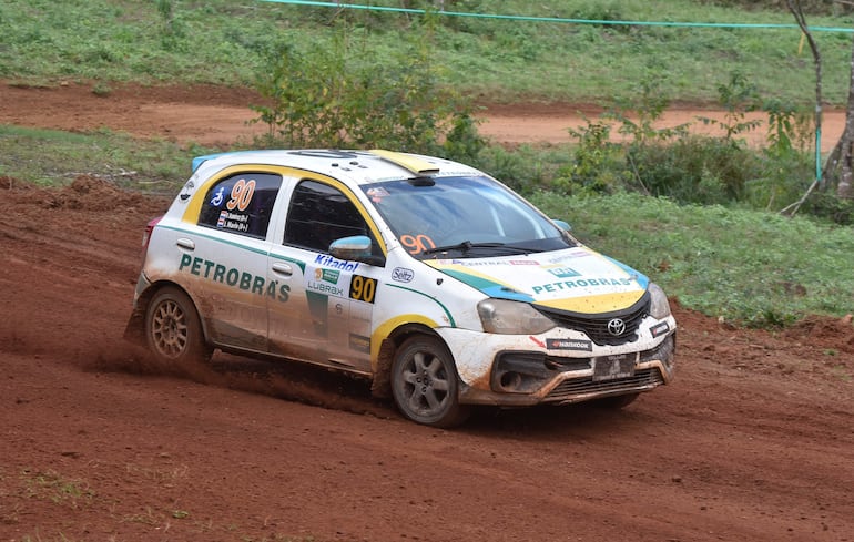 Un auto de rally Toyota número 90 tiembla en pista de tierra rodeada de vegetación.