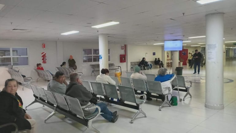 Cinco personas sentadas en sillas metálicas, esperando en un área de atención ambulatoria, con ambiente sencillo y bien iluminado.