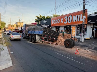 Camión de carga de ladrillos varado en la calzada, junto a ladrillos esparcidos y un vehículo detenido en un entorno urbano.