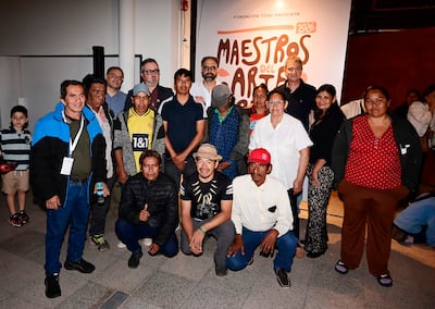 Catorce personas posan en evento, algunos llevan sombreros y abrigos, todos sonríen hacia la cámara en un ambiente interior.