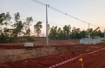 Lugar de construcción con maquinarias operando y trabajadores en chalecos naranjas en un paisaje rural con cielo nublado.