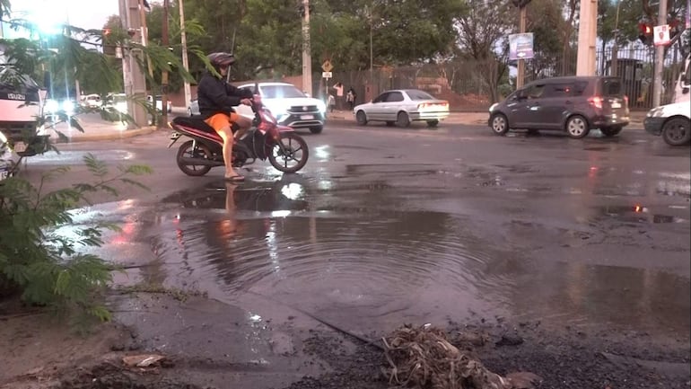 Motociclista con casco negro y chaleco oscuro observa charcos en la Avenida José Gervasio Artigas tras la lluvia.