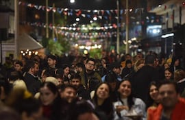 Multitud sonriente en festival nocturno, con personas en sombreros y decoraciones de colores alrededor de un espacio al aire libre.