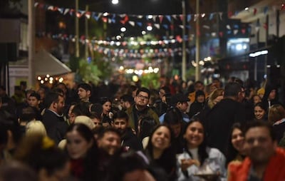 Multitud sonriente en festival nocturno, con personas en sombreros y decoraciones de colores alrededor de un espacio al aire libre.
